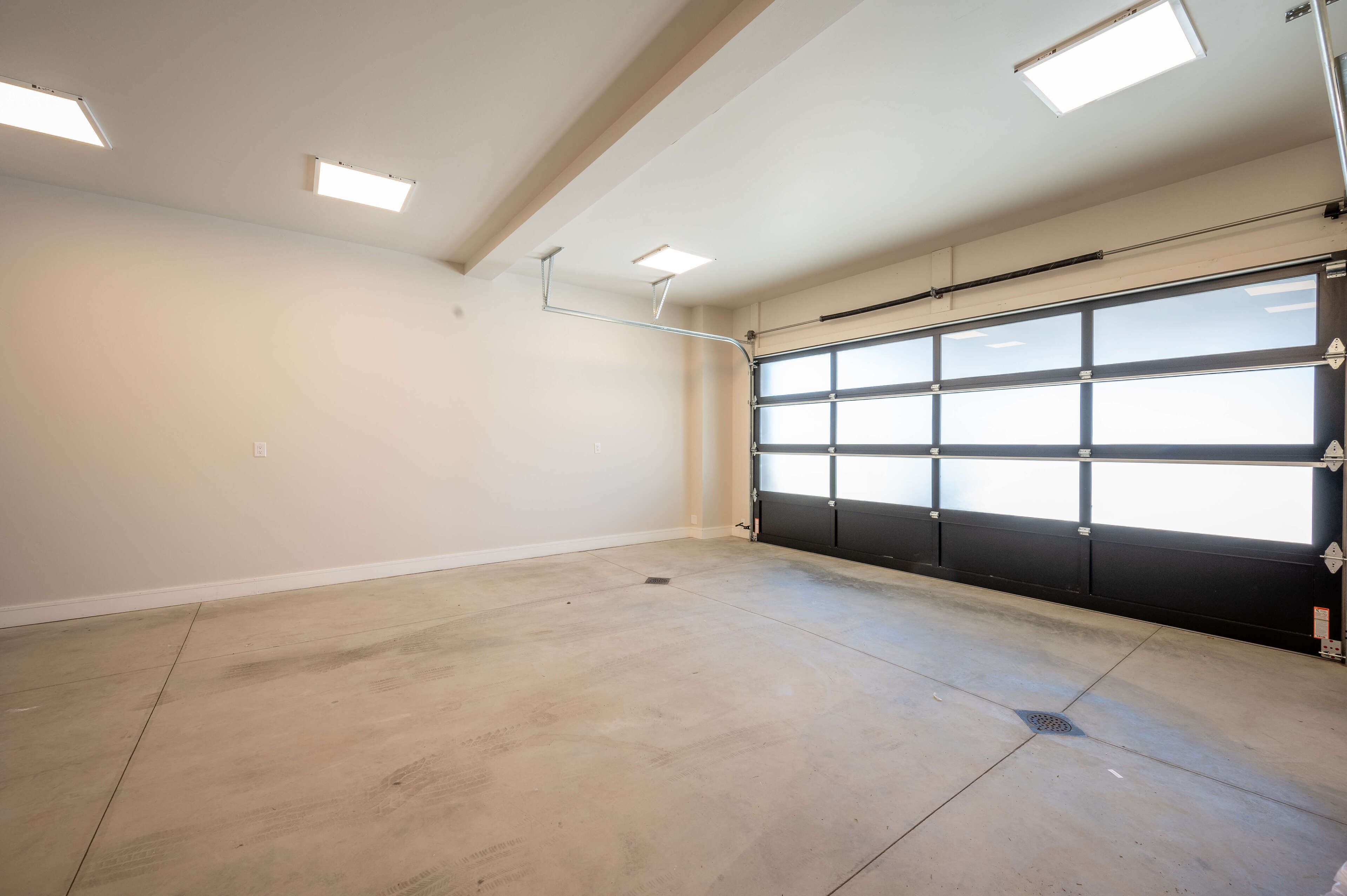 A garage with a large black garage door, a concrete floor, and three ceiling lights.