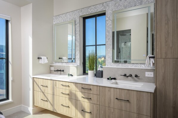 A modern bathroom with two sinks, a large mirror, and a window.