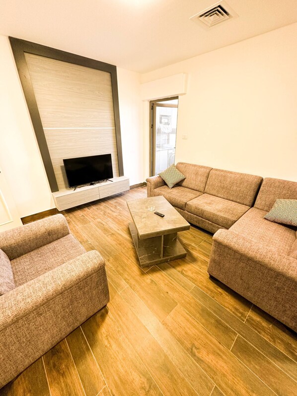 A modern living room with a sectional sofa, a coffee table, and a flat-screen TV mounted on a wall.