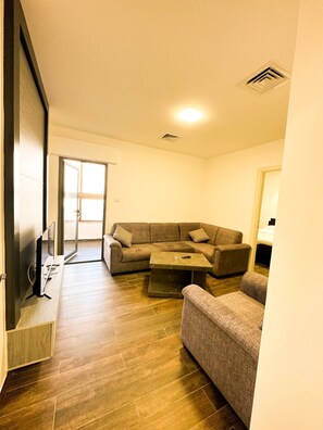 A living room with a sectional sofa, a coffee table, and a flat-screen TV. - Central Apartment For Rent 28 (Amman)