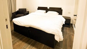 A bedroom with a bed, a chair, a bedside table, and a door.