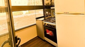 A kitchen with a gas stove, a white refrigerator, and a large window offering a view of buildings outside.