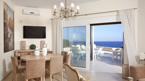 Ein modernes Wohnzimmer mit Essbereich, einem Fernseher und einer großen Schiebeglastür, die auf einen Balkon mit Pool und Meerblick führt.
