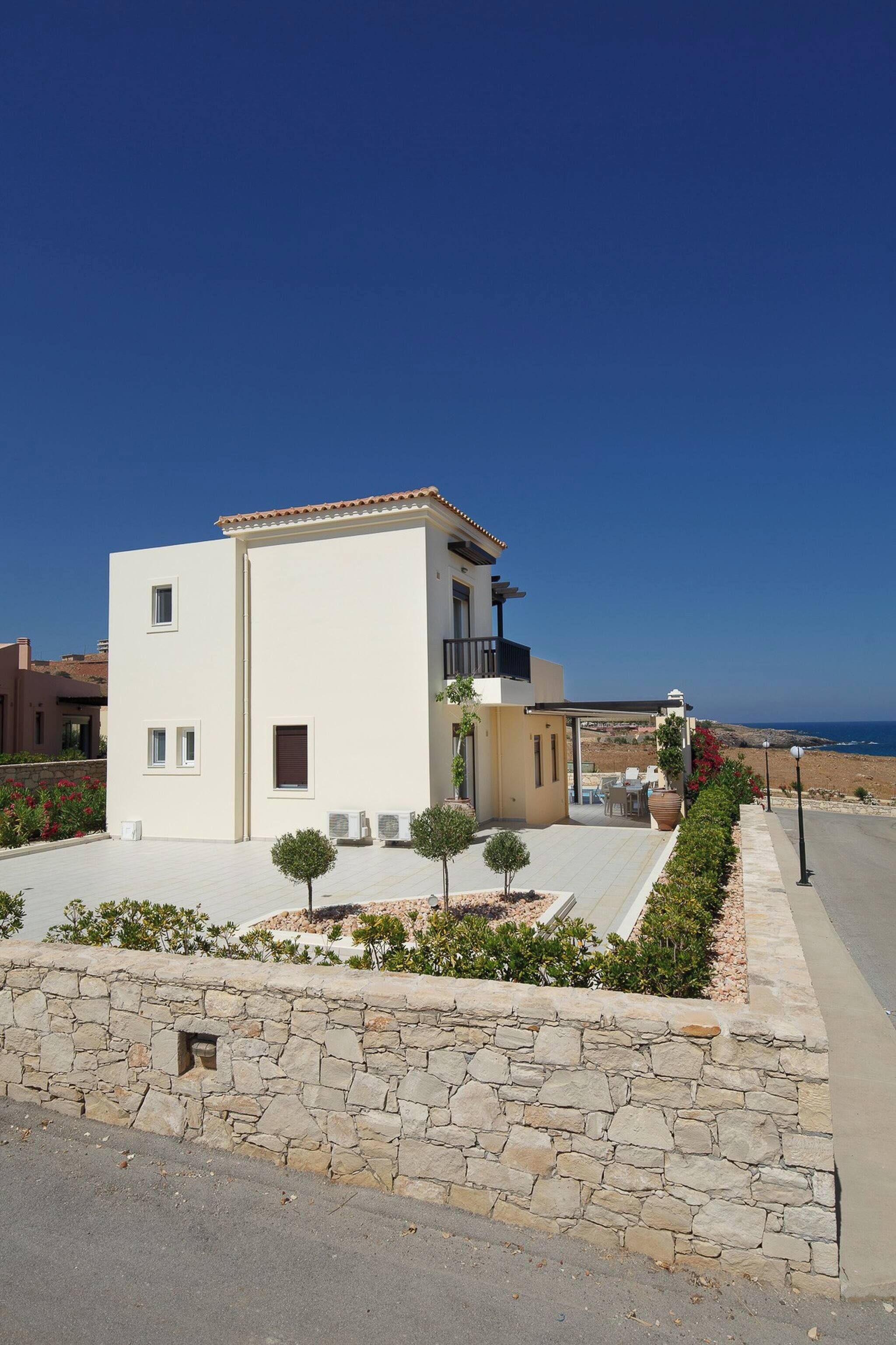 Une maison moderne à deux étages, dotée d’un balcon, d’un mur en pierre à l’avant et offrant une vue sur la mer.