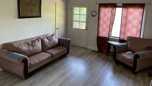 A room with a patterned sofa, a smaller chair, a small table, and a door with a window.