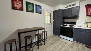 A kitchen with a bar stool set, a stove, and three paintings on the wall.