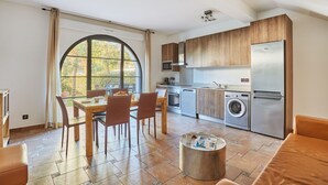 A modern kitchen with wooden cabinets, a stainless steel refrigerator, and a dining area with a table and chairs.