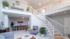 Un vaste espace de vie comprenant un escalier, un coin repas et un espace détente avec un canapé et des fauteuils.