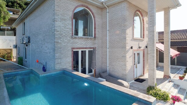 Une maison à deux étages dotée d’une piscine, d’un patio couvert et d’une façade en briques.