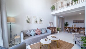 Un salon moderne avec un canapé gris, deux tables en marbre blanc et un coin repas avec des chaises en bois.