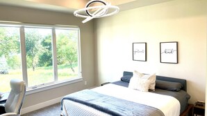 A bedroom with a large window, a bed with a blue and white quilt, two framed pictures on the wall, and a chair. - Eagles' View Retreat! Family-sized home in Texas countryside with stunning views (Gordon)