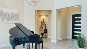 A grand piano in a spacious room with a wooden floor, a chandelier, and a door with a modern design. - Eagles' View Retreat! Family-sized home in Texas countryside with stunning views (Gordon)