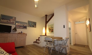 Una sala de estar con televisor, mueble de madera, sofá rojo y un comedor con sillas y mesa.