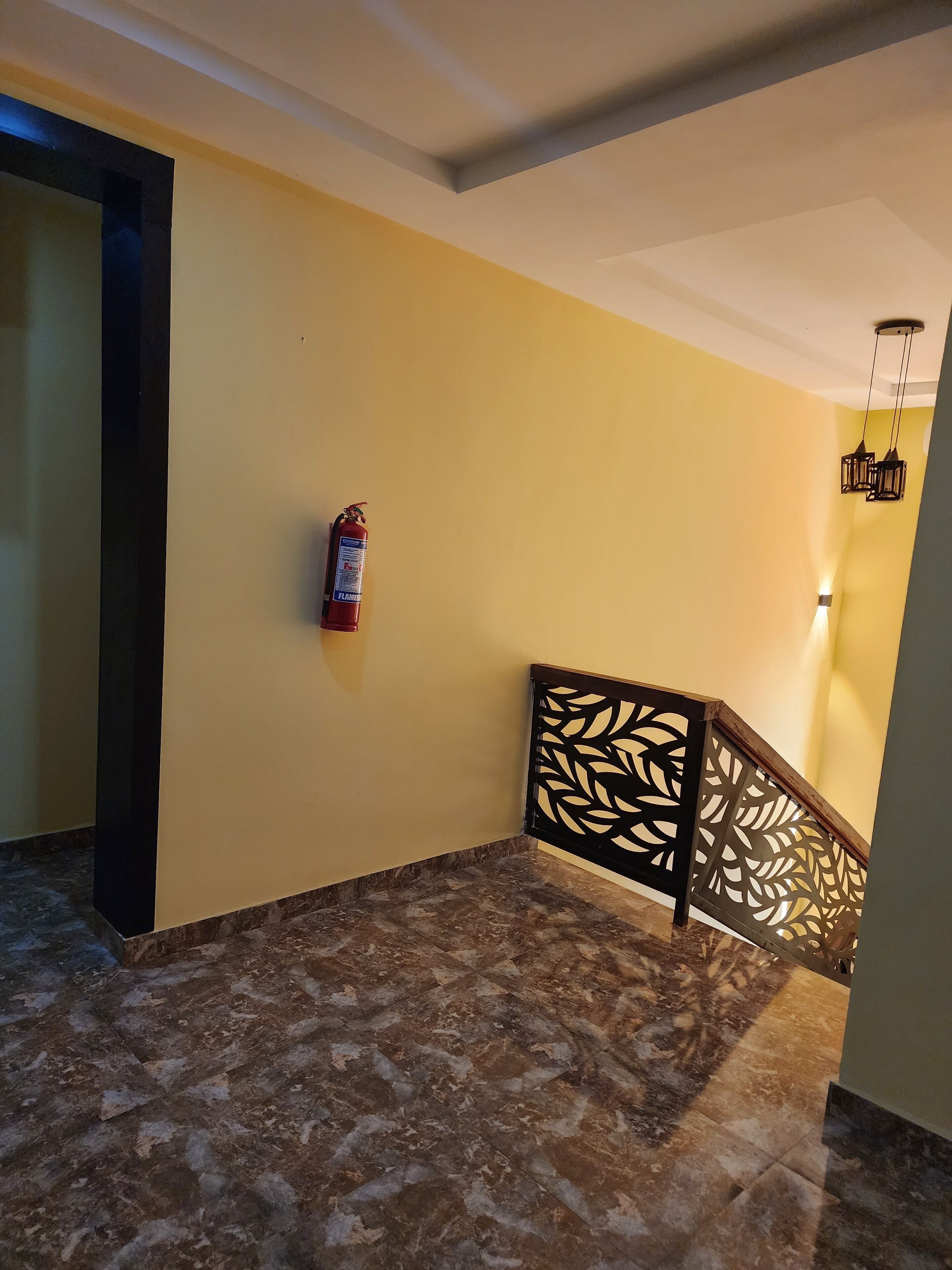 A hallway with a fire extinguisher mounted on the wall, a patterned railing, and a marble floor.