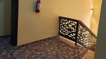 A hallway with a fire extinguisher mounted on the wall, a patterned railing, and a marble floor.