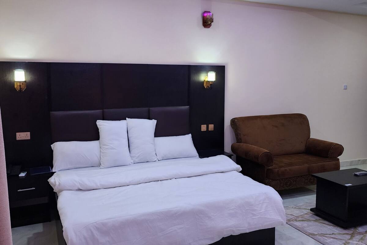 A modern bedroom with a large bed, a brown armchair, and a small table.