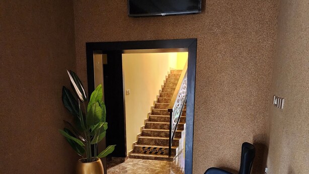 A modern interior with a staircase leading to a second floor, a large potted plant, and a seating area with two chairs and a small table. - The 401 Hotel and Suites Awka (Awka)