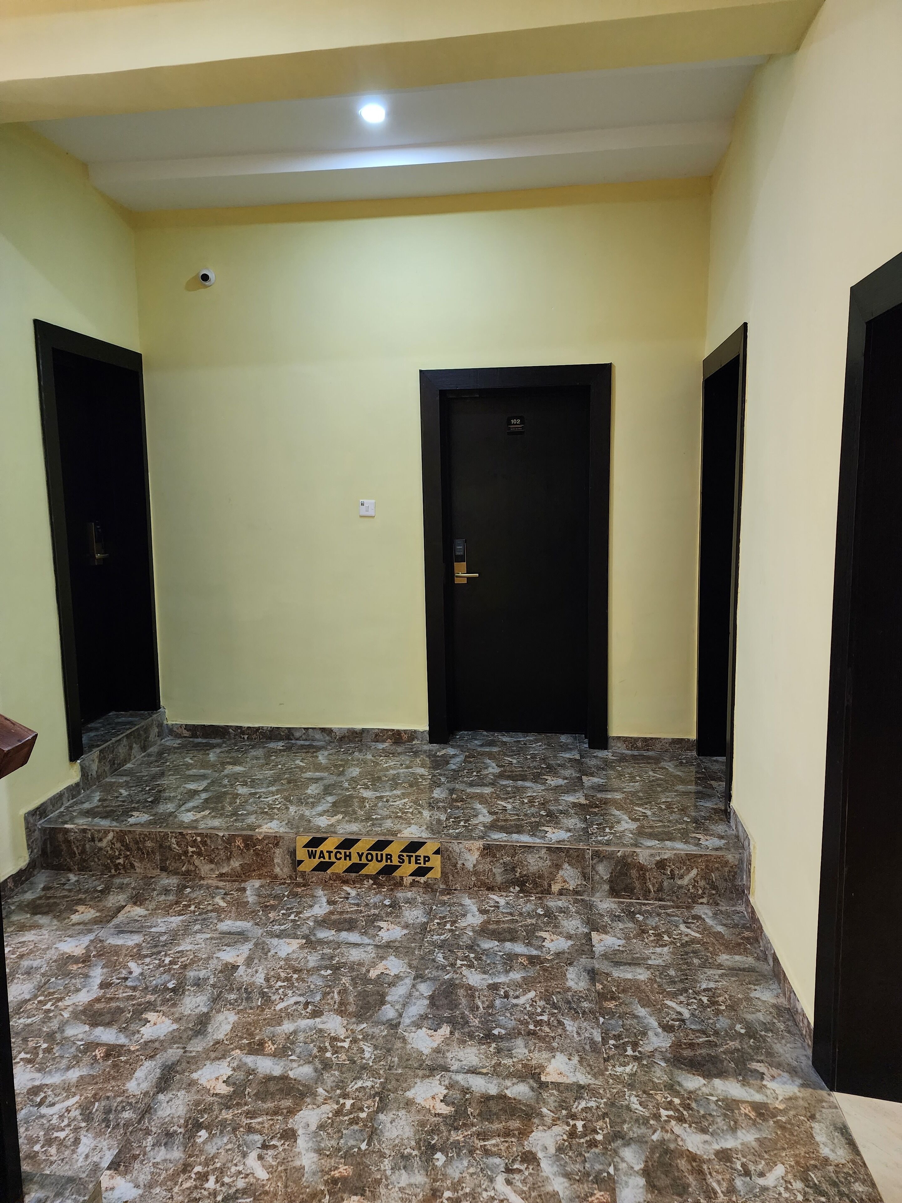 A hallway with marble flooring, a warning sign, and three doors.