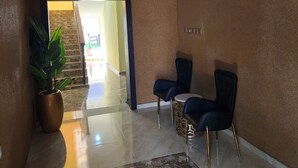 A hotel lobby with a TV mounted on the wall, a potted plant, two chairs, and a marble floor. - The 401 Hotel and Suites Awka (Awka)