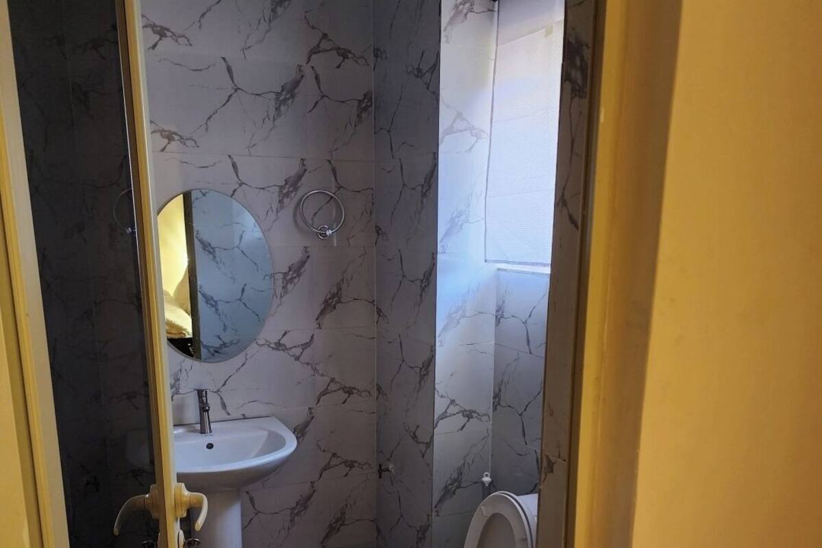 A bathroom with a marble wall, a sink, a toilet, and a window.