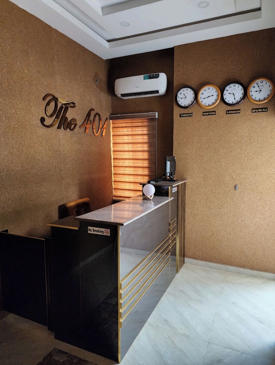 A reception desk with a 'No Smoking' sign, a wall-mounted air conditioner, and clocks displaying times for Toronto, New York, London, and Dubai.