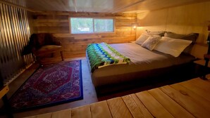 Una habitación de cabaña acogedora con una cama, un ventanal, una silla y una alfombra.