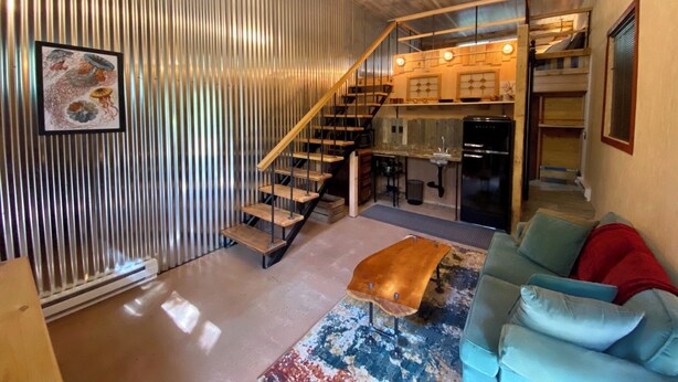 Un interior moderno con una escalera, una zona de cocina y una sala de estar con sofá y una mesa de centro.