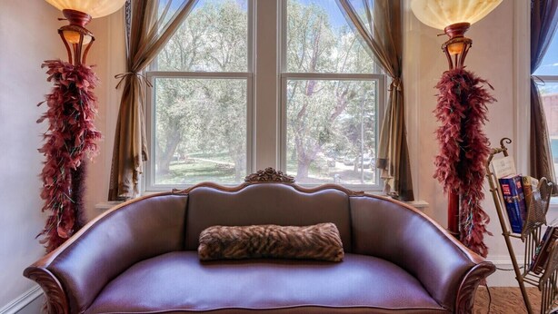A room with a leather sofa, two lamps with feathered decorations, and a view of trees through a window. - Dog Friendly- Downtown - Historic Palace Hotel Condos- Suite 202 (Salida)
