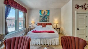 A hotel room with a large bed, two bedside tables, a painting above the bed, a window with curtains, and a door. - Dog Friendly- Downtown - Historic Palace Hotel Condos- Suite 202 (Salida)
