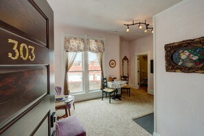 Una habitación con un ventanal grande, una zona de comedor con mesa y sillas, un espejo y una puerta con un número.