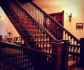 Una imponente escalera con barandales ornamentados, barandilla de madera y un rellano alfombrado.