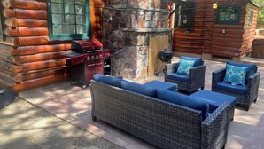 Une cabane en rondins avec une cheminée en pierre, un espace salon extérieur et un barbecue.