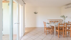 A dining area with a white table and wooden chairs, a small decorative item on the wall, and a sliding glass door leading to an outdoor area. - Elegant Residence Ea Bianca 4 Bedroom Apartment Sleeps 8 Extra bed Available (Arzachena)