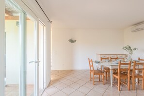 Un comedor con mesa blanca y sillas de madera, un pequeño objeto decorativo en la pared, y un ventanal corredero que da a un espacio exterior.