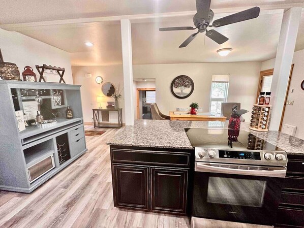 A modern kitchen with granite countertops, a built-in oven, and a dining area with a table and chairs.