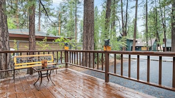 A wooden deck with a bench and railing, surrounded by tall trees and a view of a road.