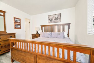 A bedroom with a wooden bed, a dresser, a nightstand, and a wall-mounted lamp.