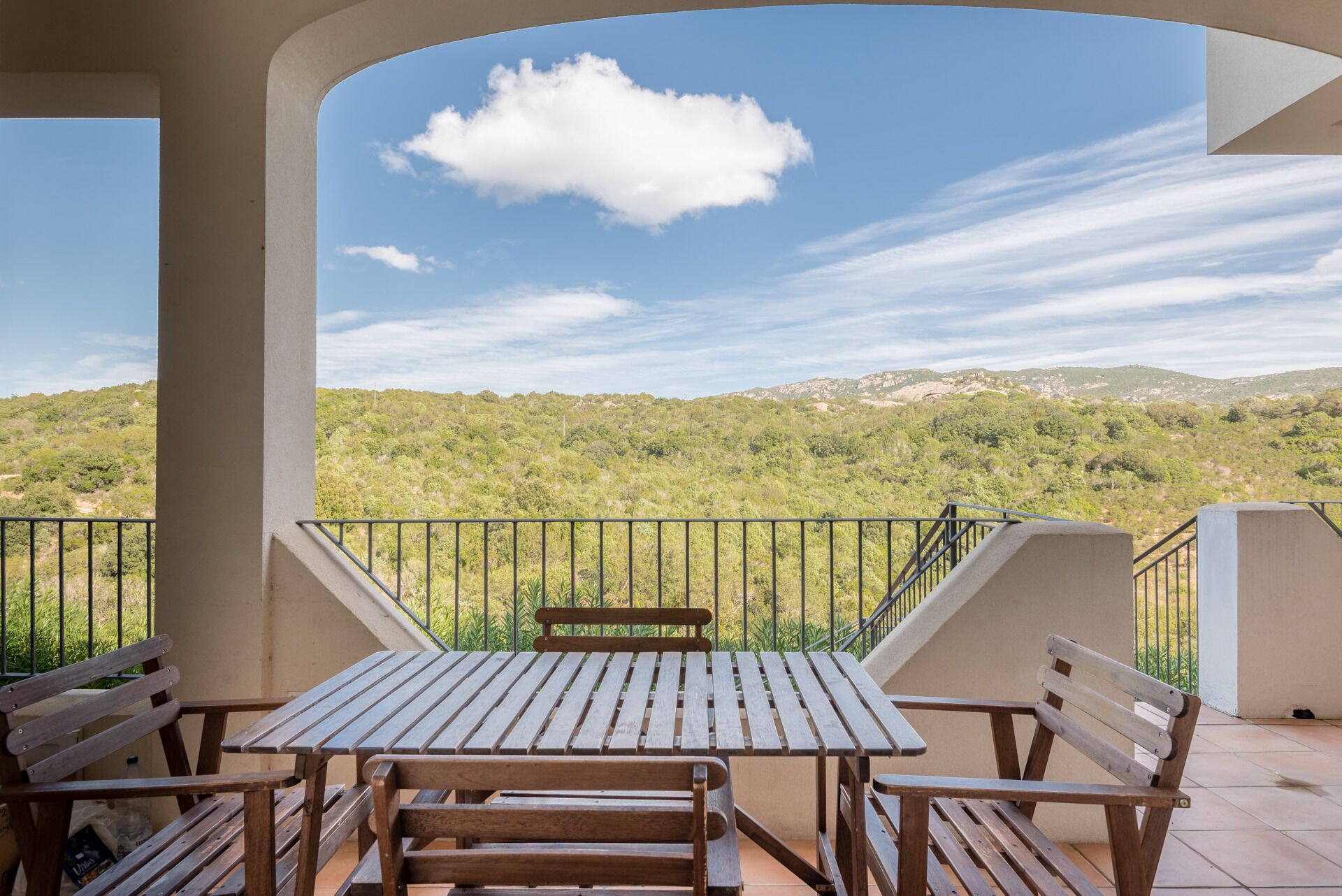 A balcony with a wooden table and benches, offering a view of a hilly landscape.