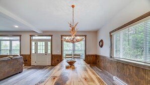 A spacious room with a large wooden dining table, a chandelier, and large windows with blinds. - Lucky Buck by PMR, 7BR Luxury Cabin, Lake View, EV Charge, Sleeps 22 (Lake Harmony)