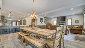 A spacious living area with a wooden dining table, benches, and a large chandelier. - Lucky Buck by PMR, 7BR Luxury Cabin, Lake View, EV Charge, Sleeps 22 (Lake Harmony)