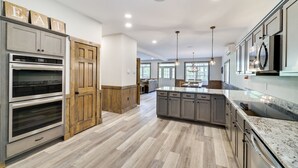 A modern kitchen with built-in ovens, a large island, and wooden cabinetry. - Lucky Buck by PMR, 7BR Luxury Cabin, Lake View, EV Charge, Sleeps 22 (Lake Harmony)