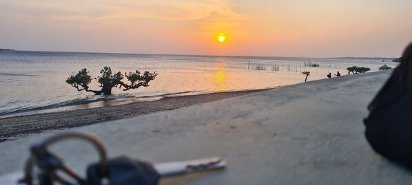 Une plage au coucher du soleil, avec une mer calme et quelques personnes.