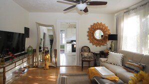 A living room with a sofa, a television, a ceiling fan, and a large mirror.