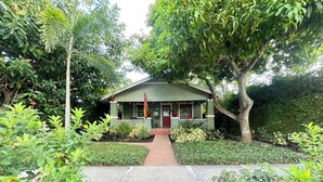 A small, green-roofed building surrounded by lush greenery and a brick pathway leading to it.