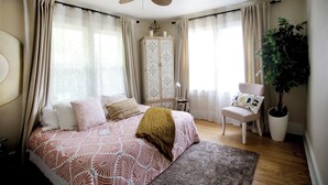 A bedroom with a bed, a chair, a potted plant, a wardrobe, and a ceiling fan.