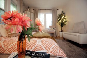 Ein Wohnzimmer mit einer Couch, einer dekorativen Vase mit Blumen und einem Weihnachtsbaum mit Lichterkette.