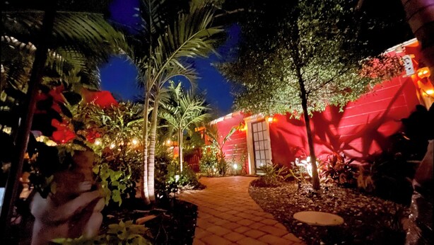 A nighttime garden pathway leading to a building with red walls and a door.