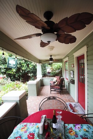 Eine überdachte Terrasse mit Esstisch, Deckenventilator und einer roten Tür.