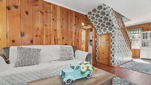 A cozy living room with a wooden wall, a sofa with patterned cushions, a small table with a toy car and flowers, and a staircase with patterned wallpaper. - Oak Nesting (Big Bear Lake)