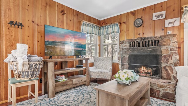 A cozy living room with wooden walls, a stone fireplace, a large painting, and a television. - Oak Nesting (Big Bear Lake)